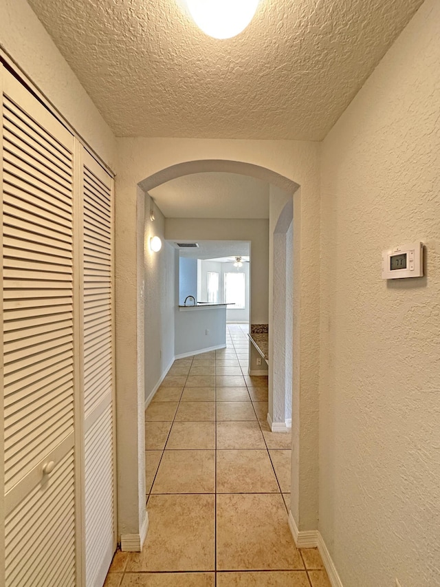 hallway featuring arched walkways, light tile patterned floors, a textured ceiling, and a textured wall