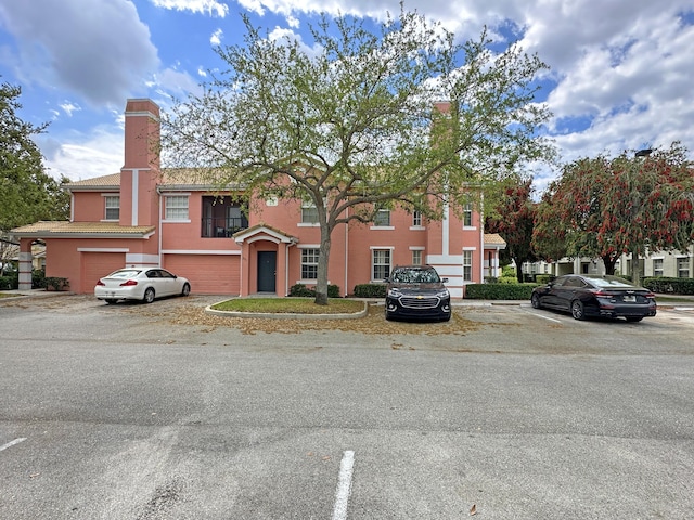 view of property featuring stucco siding, uncovered parking, a tile roof, and a chimney