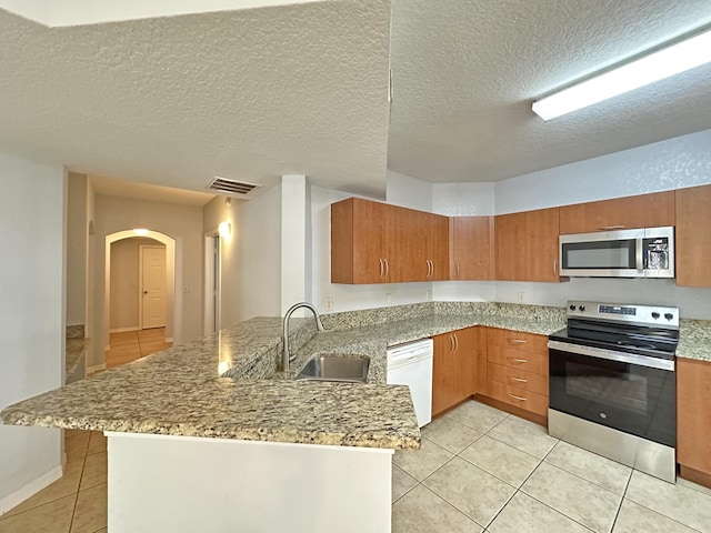 kitchen with light tile patterned floors, visible vents, a peninsula, a sink, and appliances with stainless steel finishes