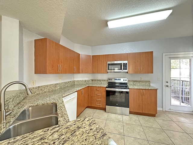 kitchen with a sink, light stone counters, brown cabinets, and appliances with stainless steel finishes