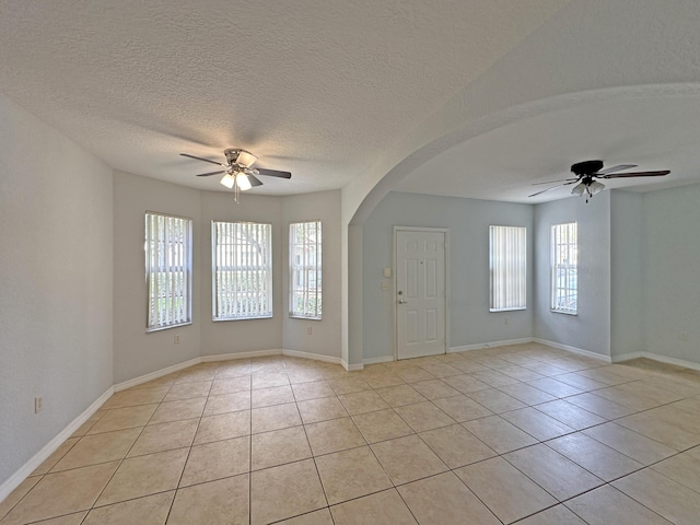 empty room with light tile patterned floors, baseboards, arched walkways, and ceiling fan