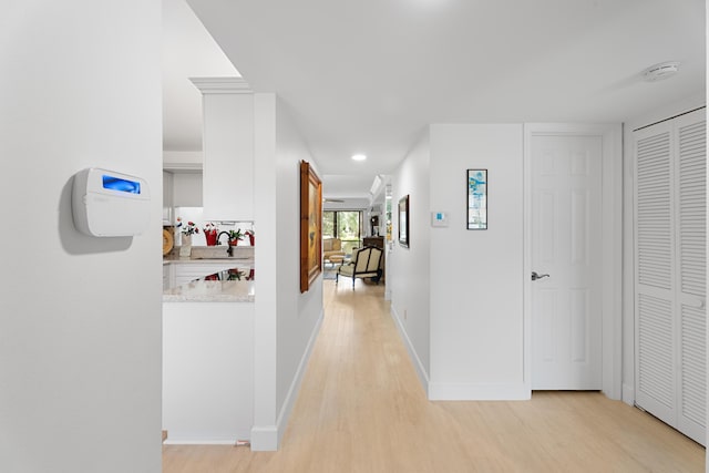 hall with a sink, baseboards, and light wood-style floors