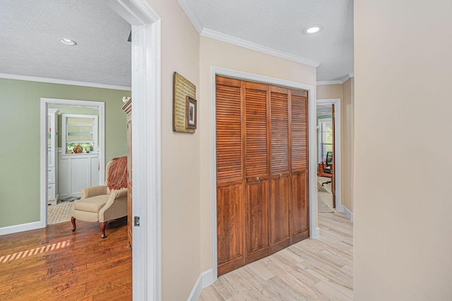 hall featuring crown molding, light wood-style flooring, a healthy amount of sunlight, and a textured ceiling