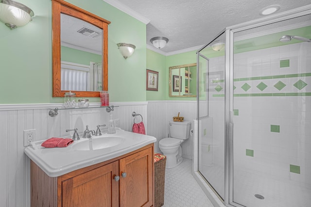 bathroom with wainscoting, ornamental molding, a shower stall, a textured ceiling, and toilet