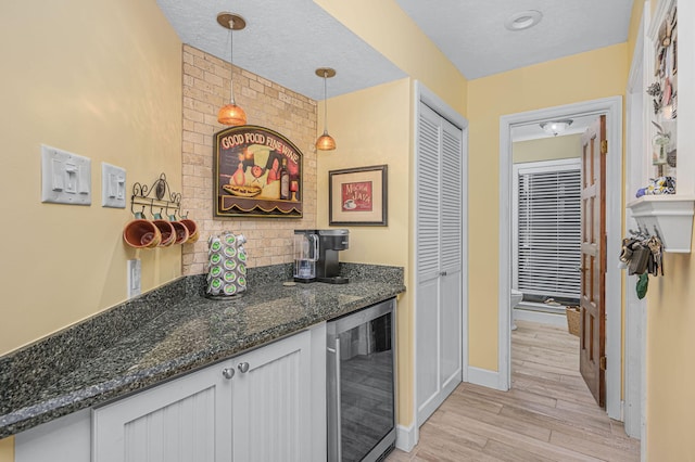 bar with beverage cooler, a bar, decorative backsplash, decorative light fixtures, and light wood-type flooring