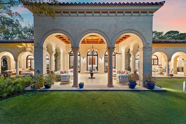 back of property at dusk with an outdoor living space, a yard, a patio, and stucco siding