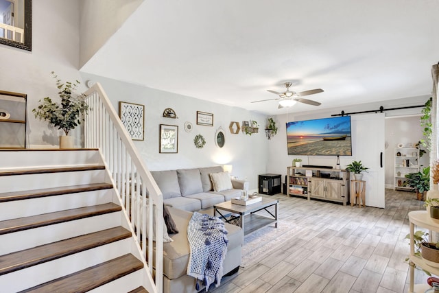 living area with a barn door, a ceiling fan, wood finished floors, and stairs