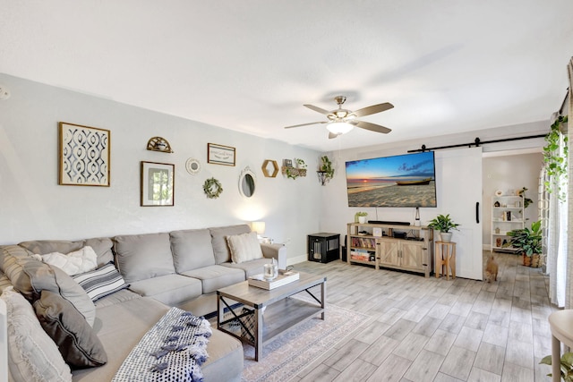 living room featuring a ceiling fan, a barn door, light wood-style floors, and baseboards