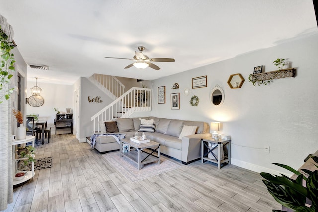 living area featuring visible vents, ceiling fan with notable chandelier, light wood finished floors, baseboards, and stairs