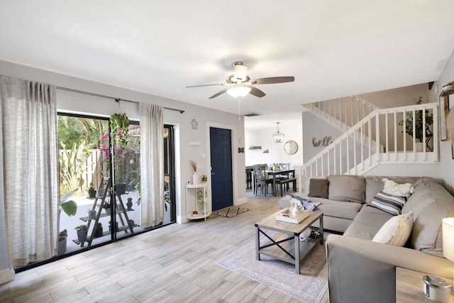 living area featuring visible vents, light wood-style flooring, stairway, baseboards, and ceiling fan