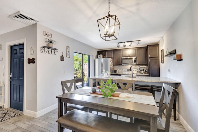 dining area featuring baseboards, visible vents, track lighting, light wood-type flooring, and a chandelier