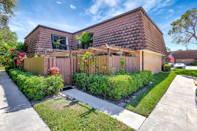 view of side of property featuring mansard roof, fence, and brick siding