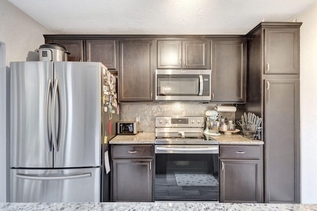 kitchen featuring light stone countertops, stainless steel appliances, dark brown cabinets, a textured ceiling, and backsplash