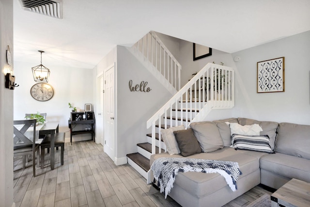 living room featuring visible vents, an inviting chandelier, light wood-style flooring, and stairs