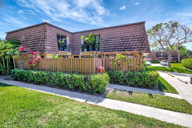 view of side of home featuring brick siding, mansard roof, fence, and a yard