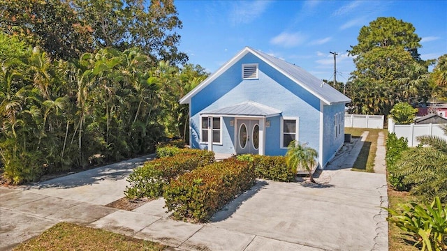 bungalow-style home with stucco siding, metal roof, and fence