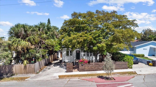 view of property hidden behind natural elements with a fenced front yard and concrete driveway