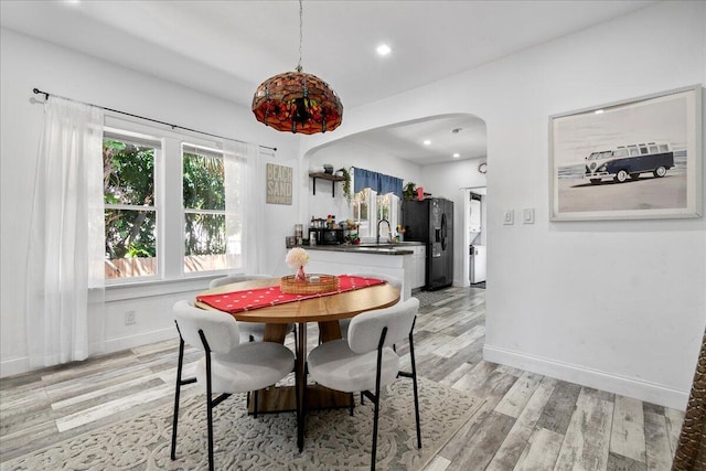 dining room with arched walkways, recessed lighting, baseboards, and light wood-style floors