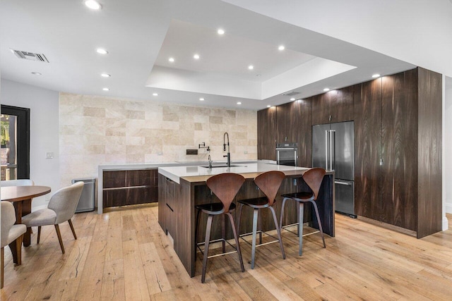 kitchen featuring a sink, appliances with stainless steel finishes, light countertops, a raised ceiling, and a large island with sink