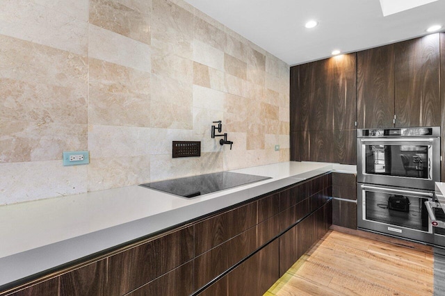 kitchen with black electric cooktop, double oven, dark brown cabinetry, and light countertops