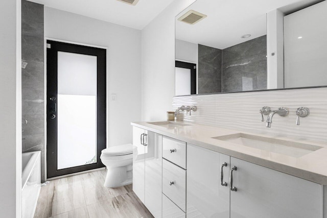 full bath with a sink, backsplash, toilet, and visible vents