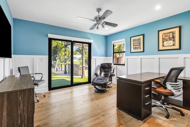 office area with a wainscoted wall, wood finished floors, a ceiling fan, and a decorative wall