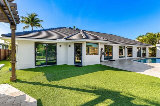 rear view of property featuring a tiled roof, a patio area, a lawn, and stucco siding