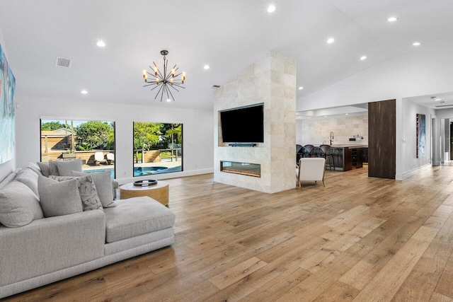 living room with visible vents, high vaulted ceiling, light wood-style floors, an inviting chandelier, and a fireplace