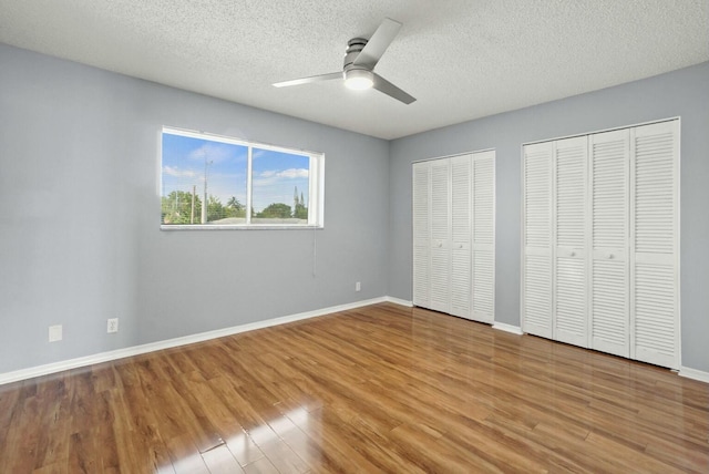 unfurnished bedroom with wood finished floors, baseboards, two closets, and a textured ceiling