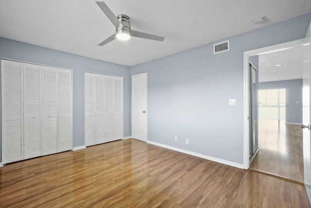 unfurnished bedroom with visible vents, multiple closets, a textured ceiling, and wood finished floors