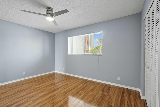 unfurnished bedroom featuring wood finished floors, baseboards, a closet, and a textured ceiling