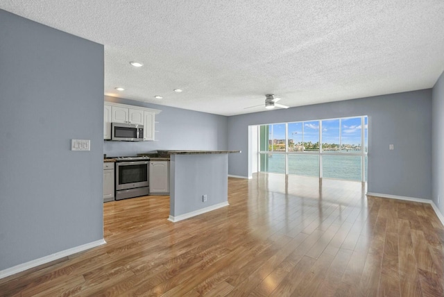 kitchen with dark countertops, baseboards, light wood-style flooring, white cabinets, and stainless steel appliances