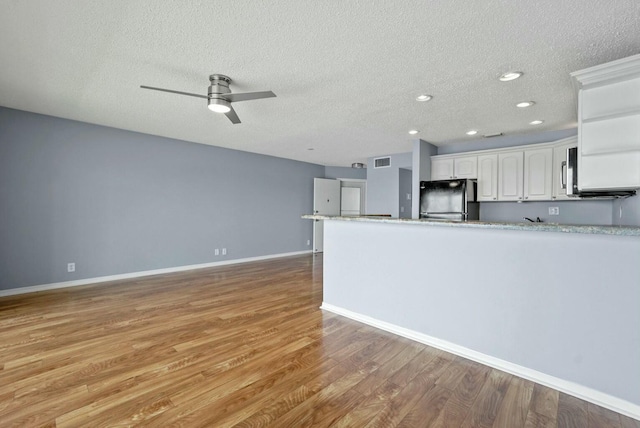 kitchen with visible vents, stainless steel microwave, white cabinetry, freestanding refrigerator, and light wood-style floors