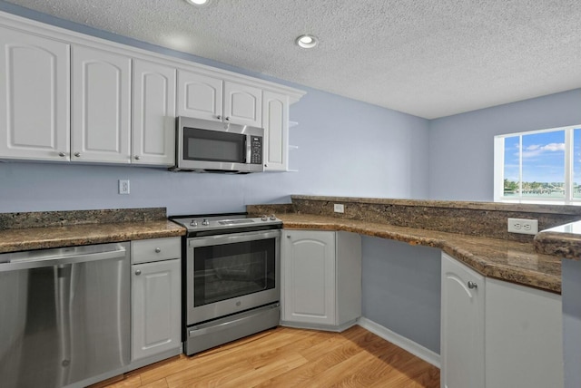 kitchen featuring light wood finished floors, dark stone counters, stainless steel appliances, a textured ceiling, and white cabinetry