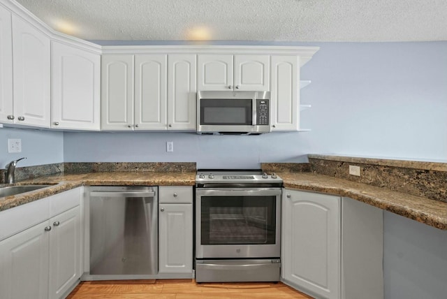 kitchen with white cabinetry, stainless steel appliances, light wood-style floors, and a sink