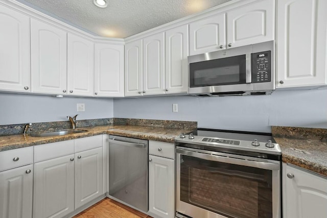 kitchen with a textured ceiling, dark countertops, white cabinets, and stainless steel appliances