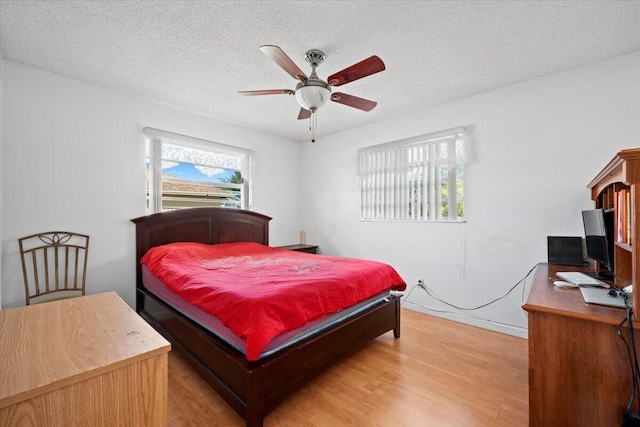 bedroom with a textured ceiling, light wood-style floors, and a ceiling fan