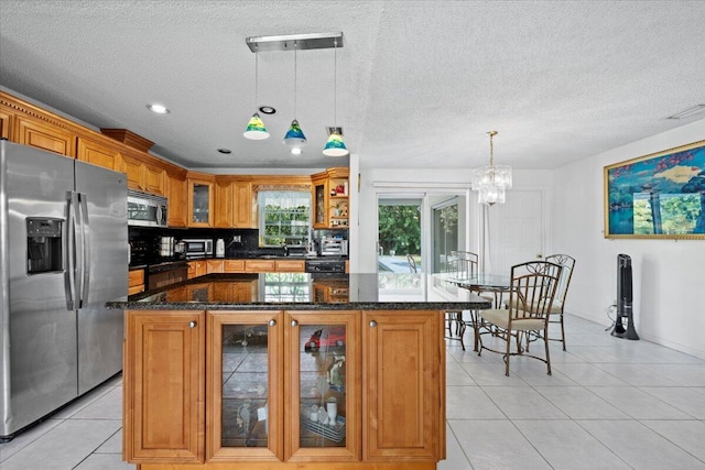 kitchen featuring brown cabinetry, dark stone counters, light tile patterned flooring, stainless steel appliances, and glass insert cabinets