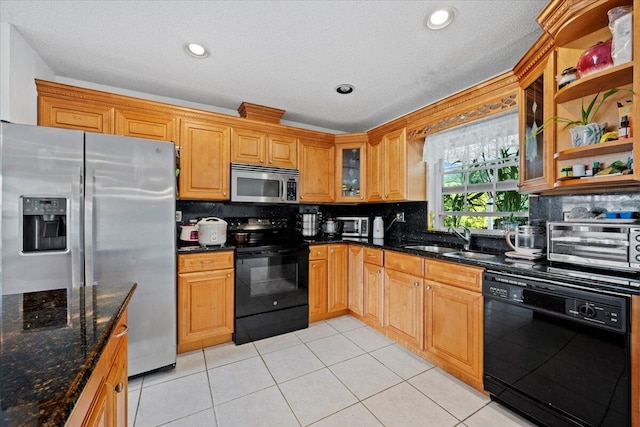 kitchen with light tile patterned floors, a sink, black appliances, glass insert cabinets, and tasteful backsplash