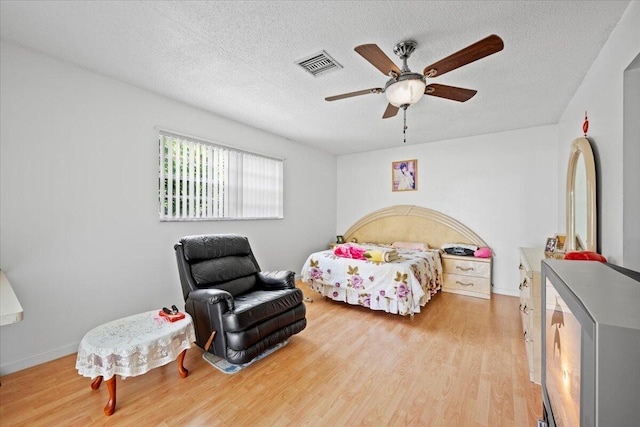 bedroom with visible vents, baseboards, ceiling fan, light wood-type flooring, and a textured ceiling