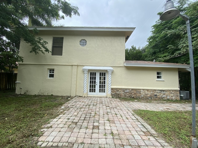 back of house with central air condition unit, stucco siding, french doors, stone siding, and a patio