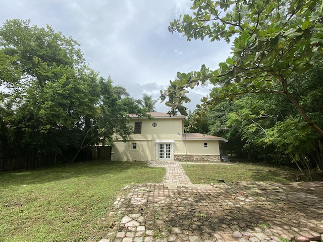 back of property featuring french doors, a lawn, stone siding, and stucco siding