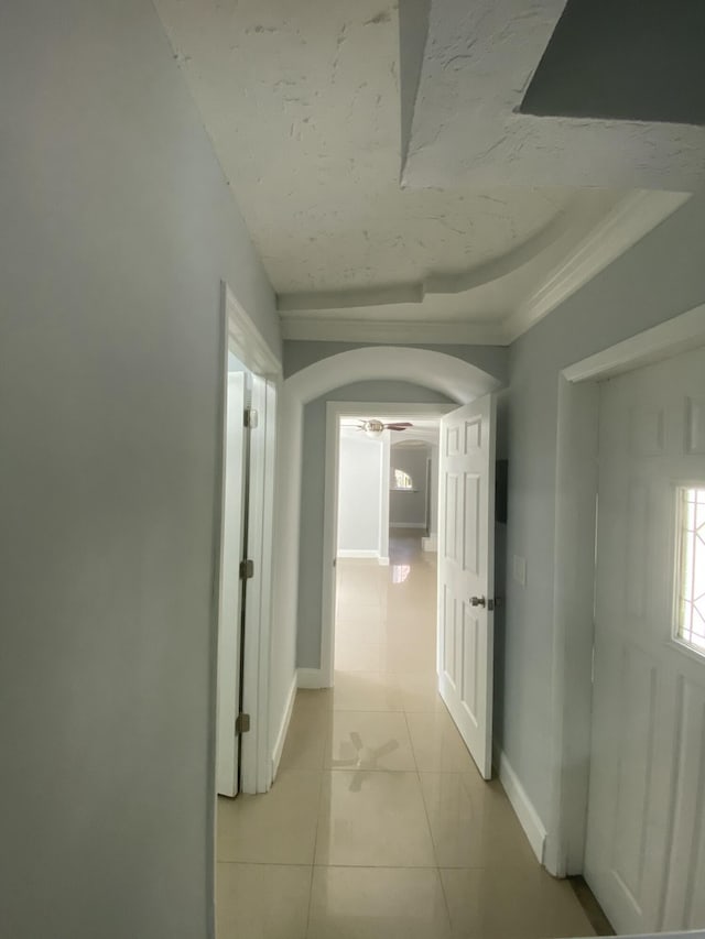 hallway with light tile patterned floors, baseboards, arched walkways, and a raised ceiling