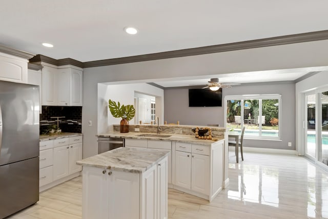 kitchen featuring tasteful backsplash, a kitchen island, ornamental molding, appliances with stainless steel finishes, and a sink