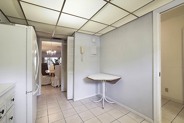 kitchen with light tile patterned floors, a drop ceiling, freestanding refrigerator, and an inviting chandelier