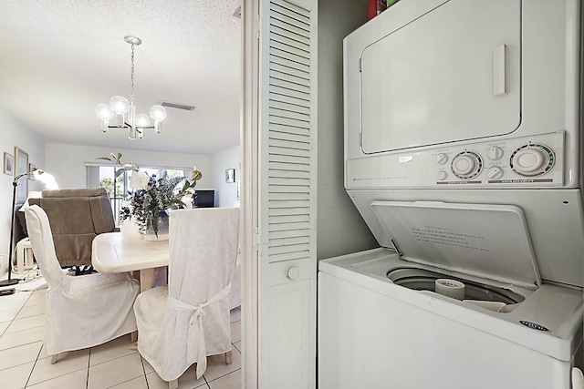 laundry area with laundry area, a notable chandelier, light tile patterned floors, and stacked washing maching and dryer