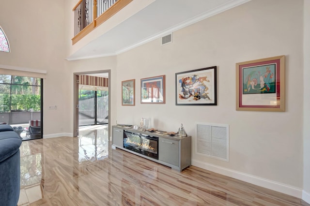 living room featuring a high ceiling, baseboards, visible vents, and ornamental molding