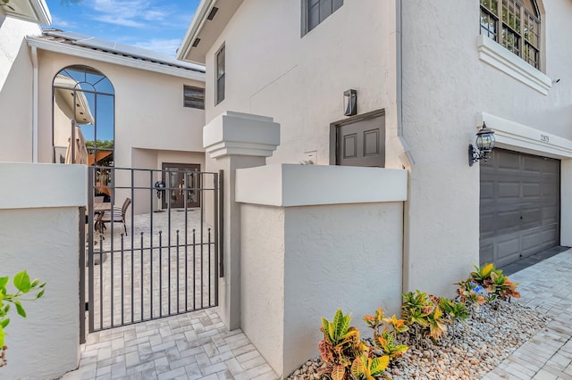 view of property exterior with stucco siding, a gate, fence, a garage, and solar panels