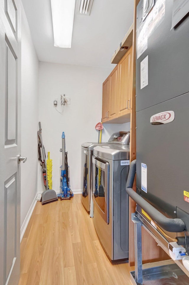 washroom featuring light wood-style flooring, cabinet space, baseboards, and washing machine and clothes dryer