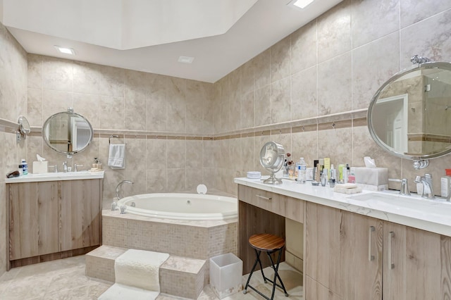 bathroom with two vanities, tile walls, a garden tub, and a sink